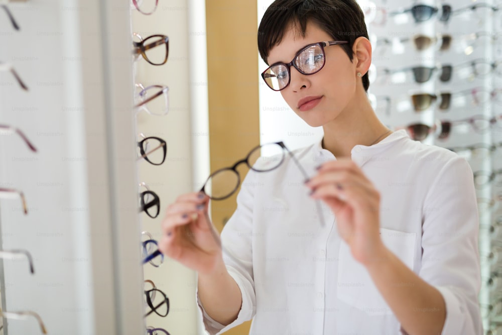 ヘルスケア、視力、視力のコンセプト - 光学ストアでメガネを選ぶ幸せな美しい女性