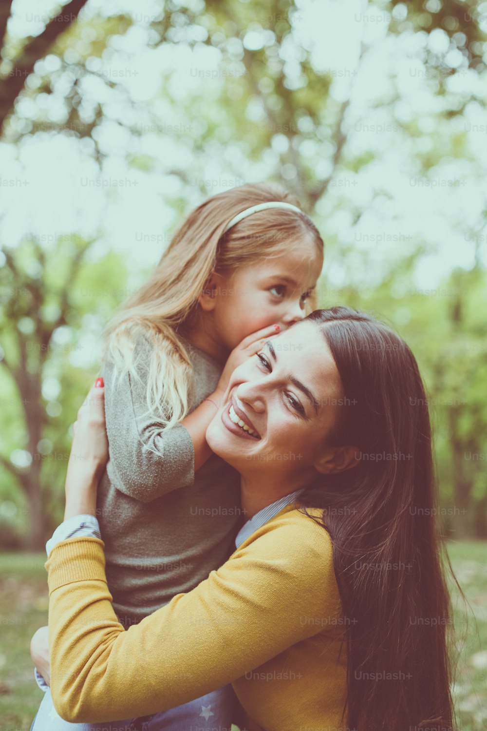Mother and daughter outdoors in a meadow. Daughter whispering to her mother secret."n