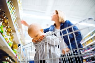 Young mother with her little baby boy at the supermarket, shopping.