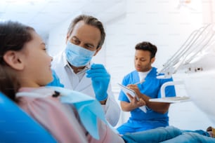 At work. Nice professional serious dentist wearing a mask and holding his instruments while preparing to start his work