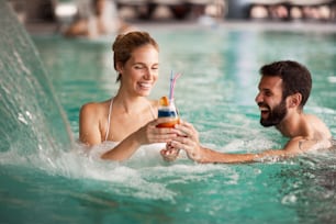 Cheerful happy couple enjoying together in swimming pool at spa center