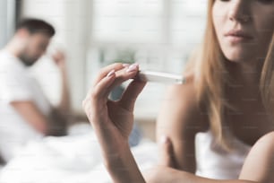 Une jeune femme pensive vérifie le résultat de son test de grossesse. Concentrez-vous sur le bâton dans sa main. L’homme nerveux est assis sur l’arrière-plan