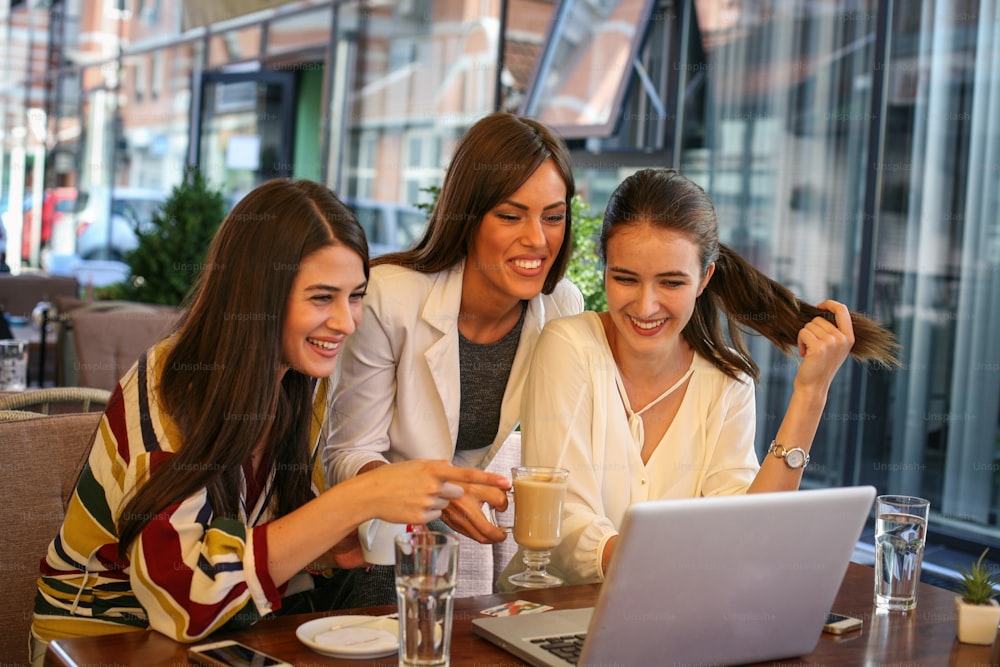 Três mulheres se divertem no laptop no café,