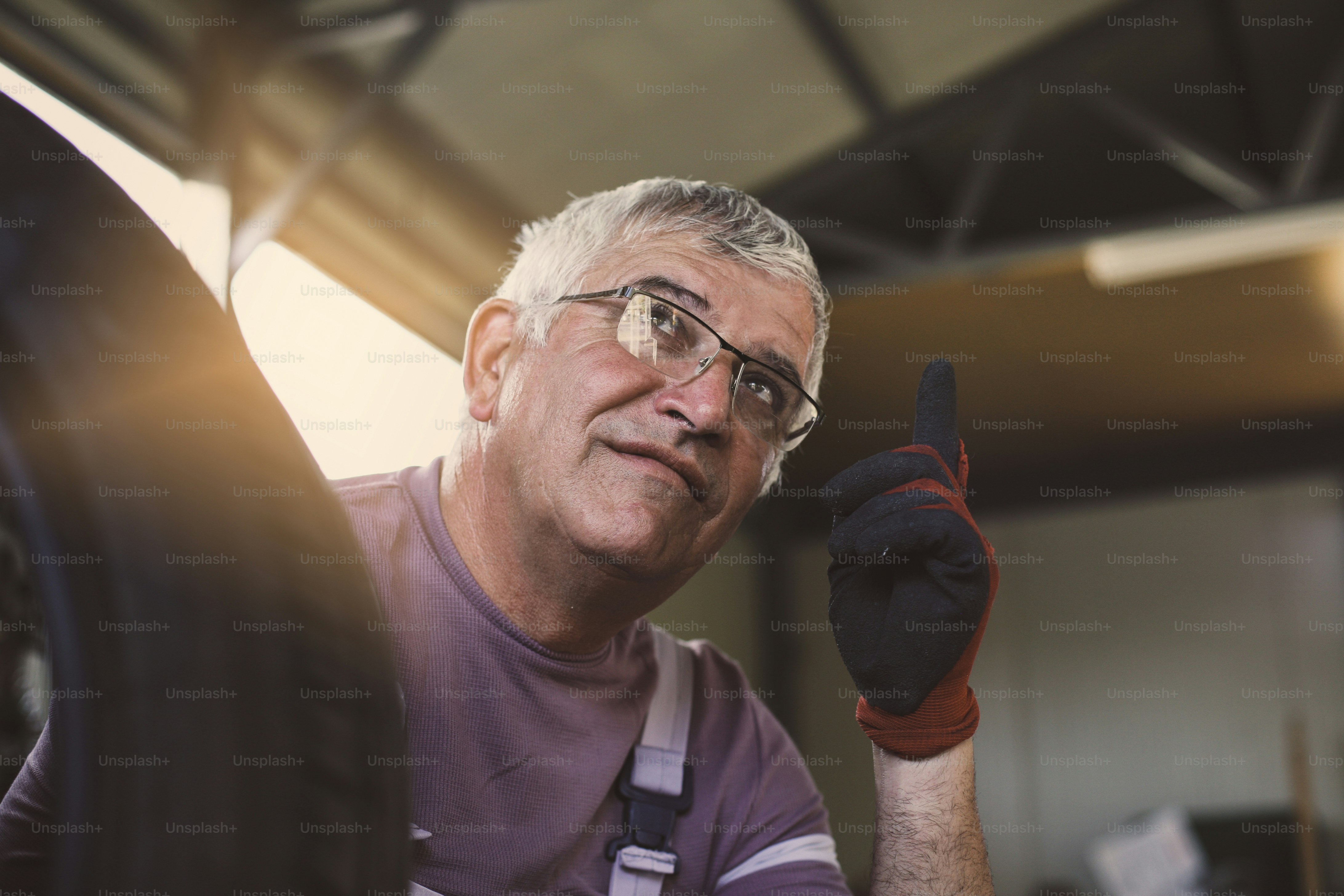 Älterer Mann in der Werkstatt. Mann sitzt nach der Arbeit mit erhobenem Finger und schaut nach oben.
