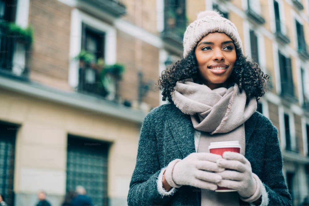 겨울에 마드리드 거리를 배회하는 커피를 마시는 젊은 흑인 여성