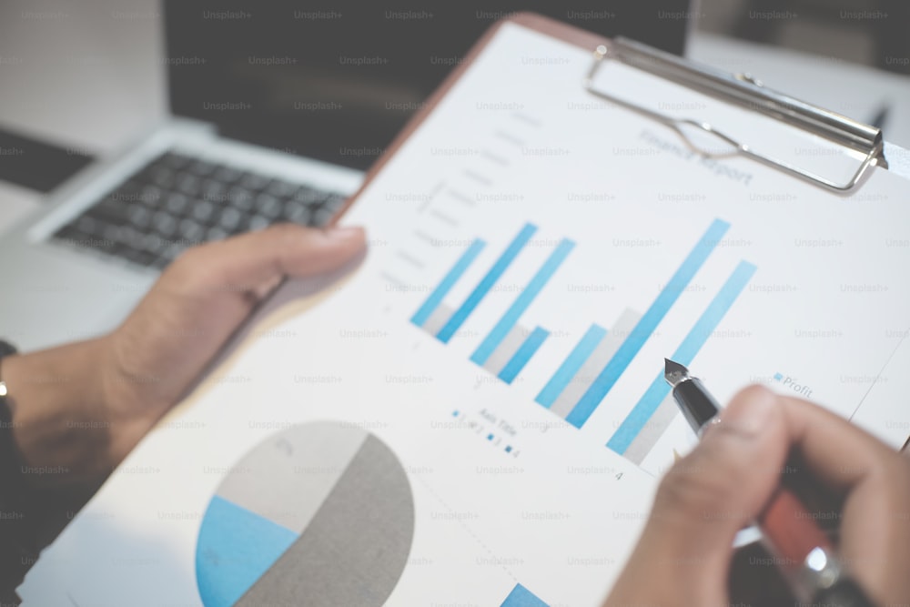 finance concept, hand pointing with pen on chart data paper of finance selective focus on pen with vintage tone.