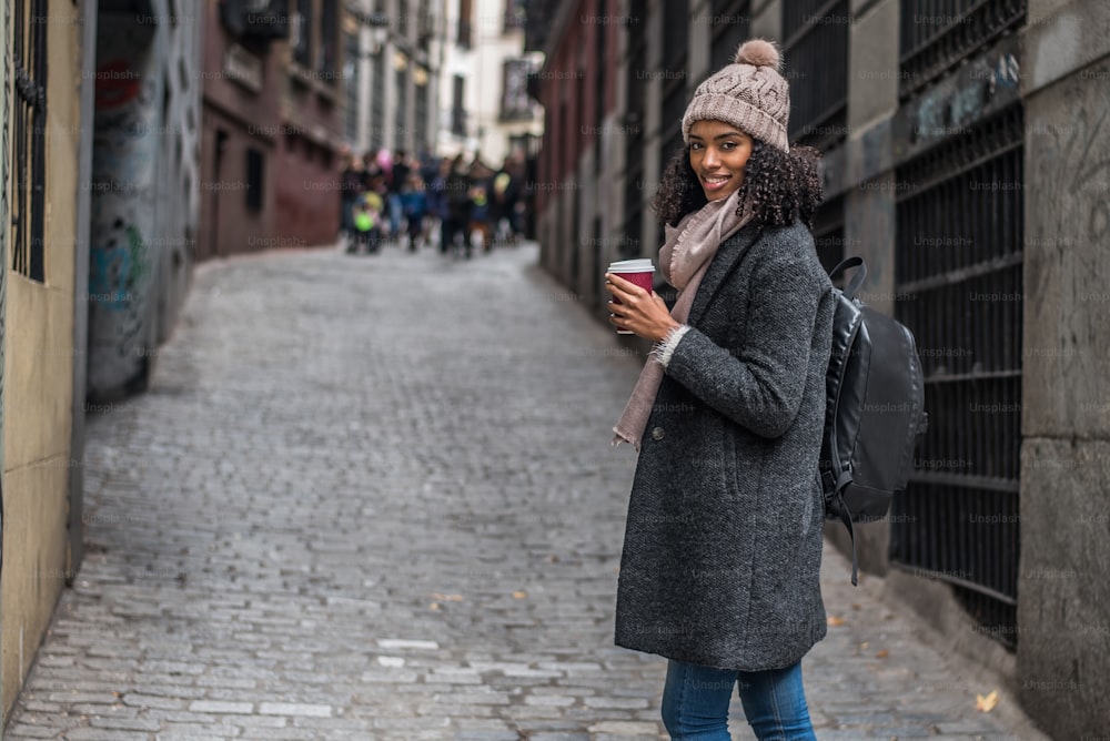 Joven negra bebiendo café deambulando por las calles de Madrid en invierno