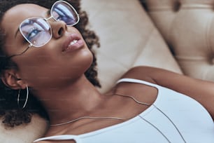 Top view of attractive young African woman looking away while lying on the sofa at home