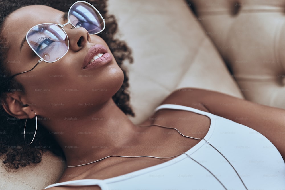 Vue de dessus d’une jeune femme africaine attrayante regardant ailleurs tout en étant allongée sur le canapé à la maison