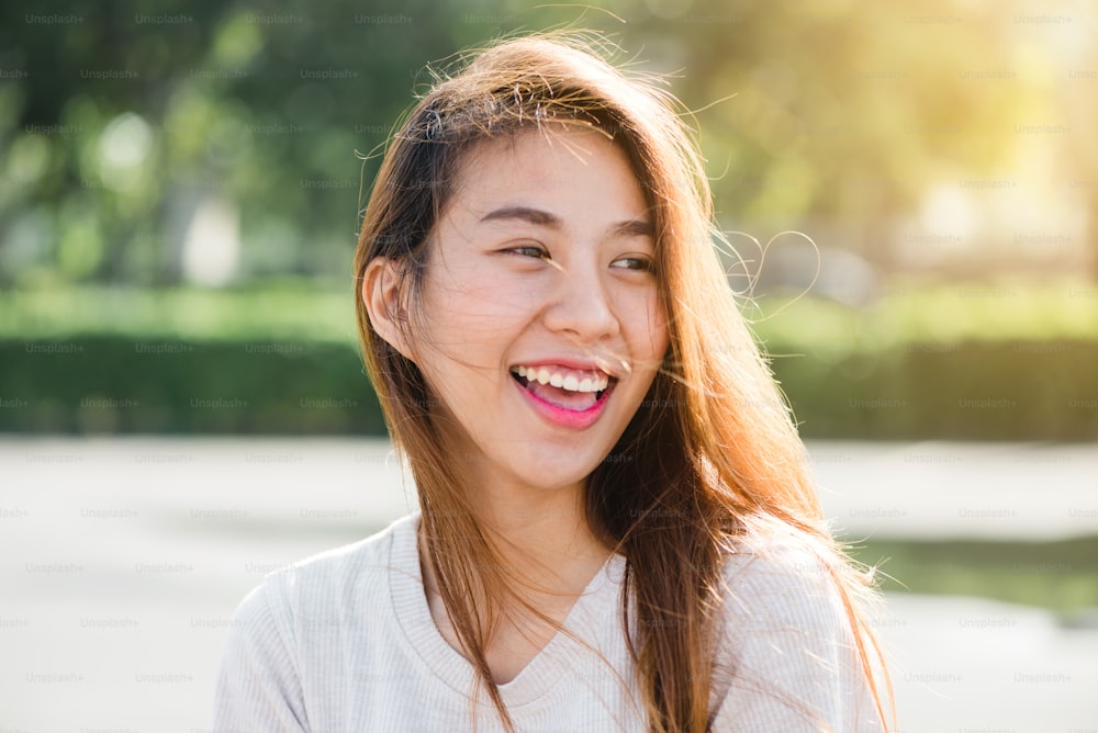 Lifestyle happy young adult asian woman smiling with teeth smile outdoors and walking on city street at sunset time. Sensual smile, stunning face. Soft colors. Lifestyle outdoors woman portrait.