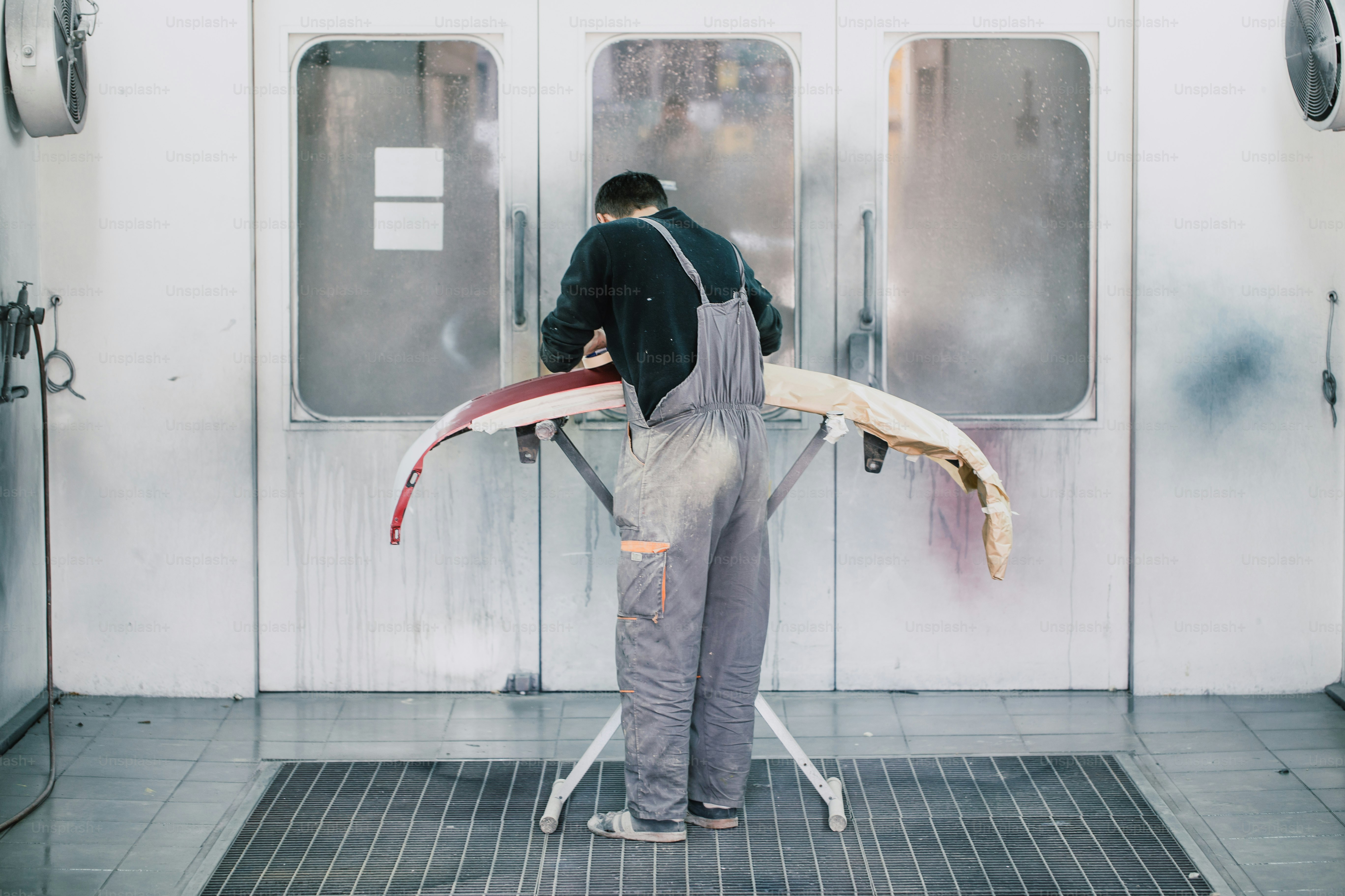 Man with protective clothes and mask painting car parts using spray compressor. Selective focus.