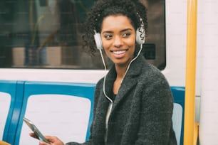 Happy young black woman sitting inside the underground listening to music
