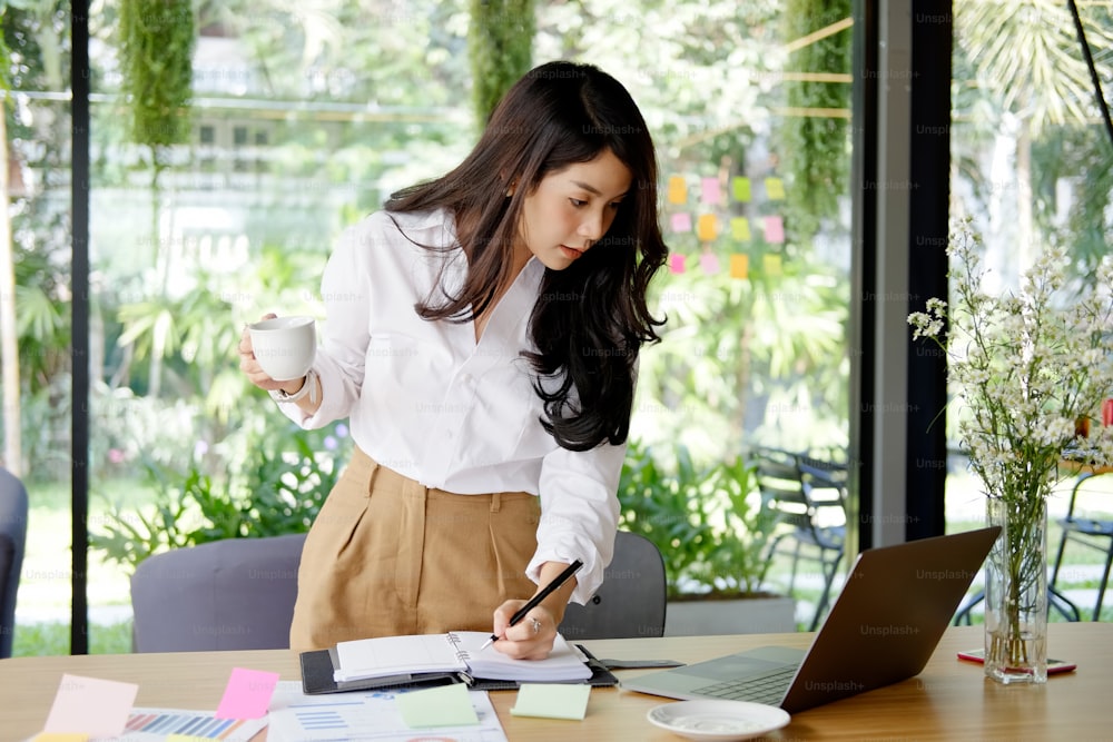 Cropped shot of a young businesswoman making notes while working on a laptop in a modern office.