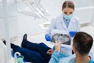 Inflamación dental. Dentista profesional y hábil sosteniendo una foto de rayos X y mirando a su paciente mientras explica el diagnóstico