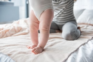 Primer plano de las piernas del bebé de pie en la cama, mujer sentada en el fondo. Enfócate en los pies