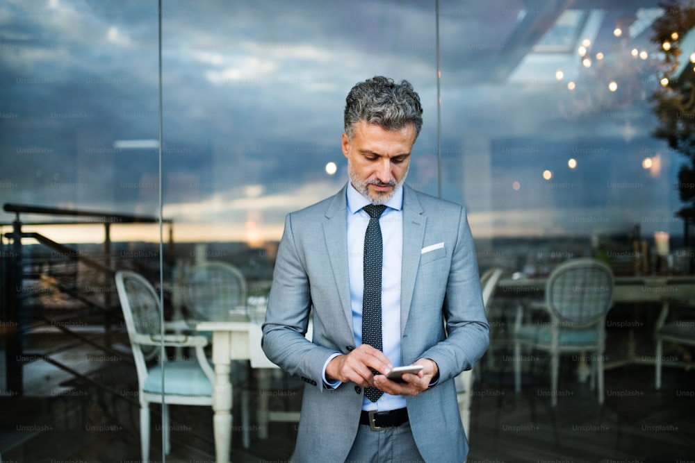 Mature businessman with smartphone standing in an outdoor hotel cafe. Man text messaging.Unrecognizable businessman with smartphone standing in an outdoor hotel cafe. Man text messaging.
