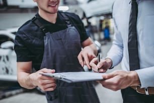 Cropped image of handsome businessman and auto service mechanic are discussing the work and signing documents. Car repair and maintenance.