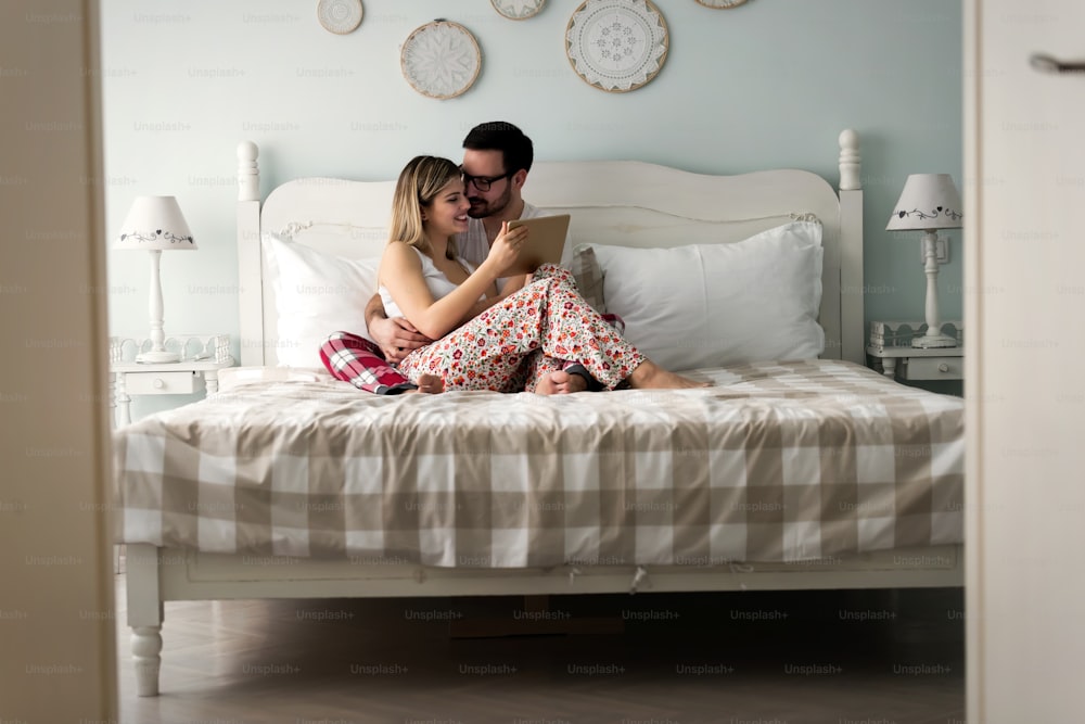 Young attractive couple using digital tablet in bedroom