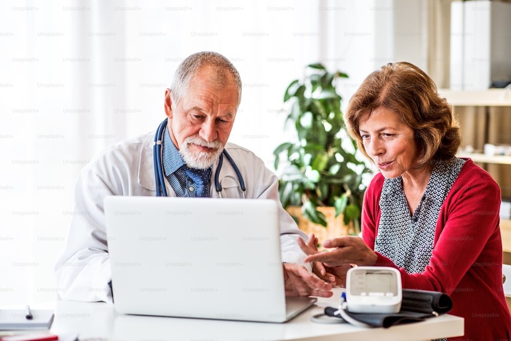 Medico maschio con laptop che parla con una donna anziana nel suo ufficio.