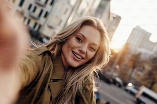 Self portrait of attractive young woman looking at camera and smiling while standing outdoors