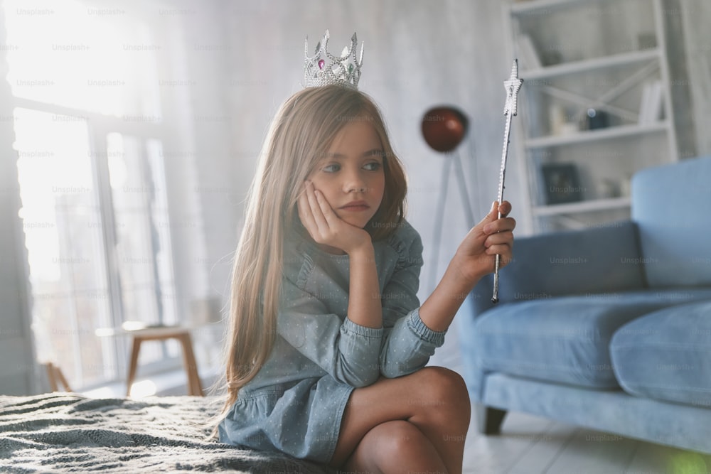 Disappointed little girl playing with a magic wand and looking away while spending time at home