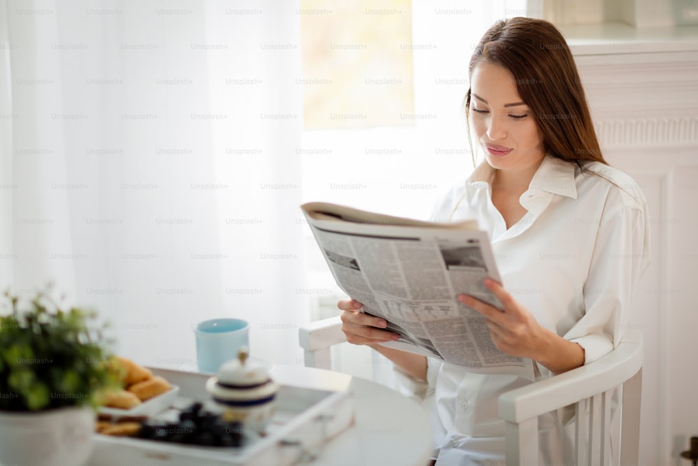 Young beautiful woman reading magazine at table in morning