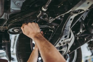 Beschnittenes Bild eines gutaussehenden Mechanikers in Uniform arbeitet im Autoservice. Autoreparatur und Wartung.