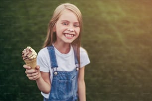 La bambina carina si diverte all'aperto. In piedi sull'erba verde e con il gelato in mano.