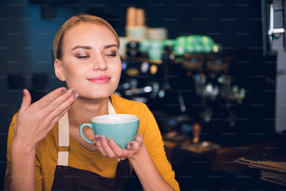 Retrato de una mujer feliz que huele apetitoso café caliente en una tienda de confitería. Ella brazo floreciente. Concepto de aroma. Espacio de copia