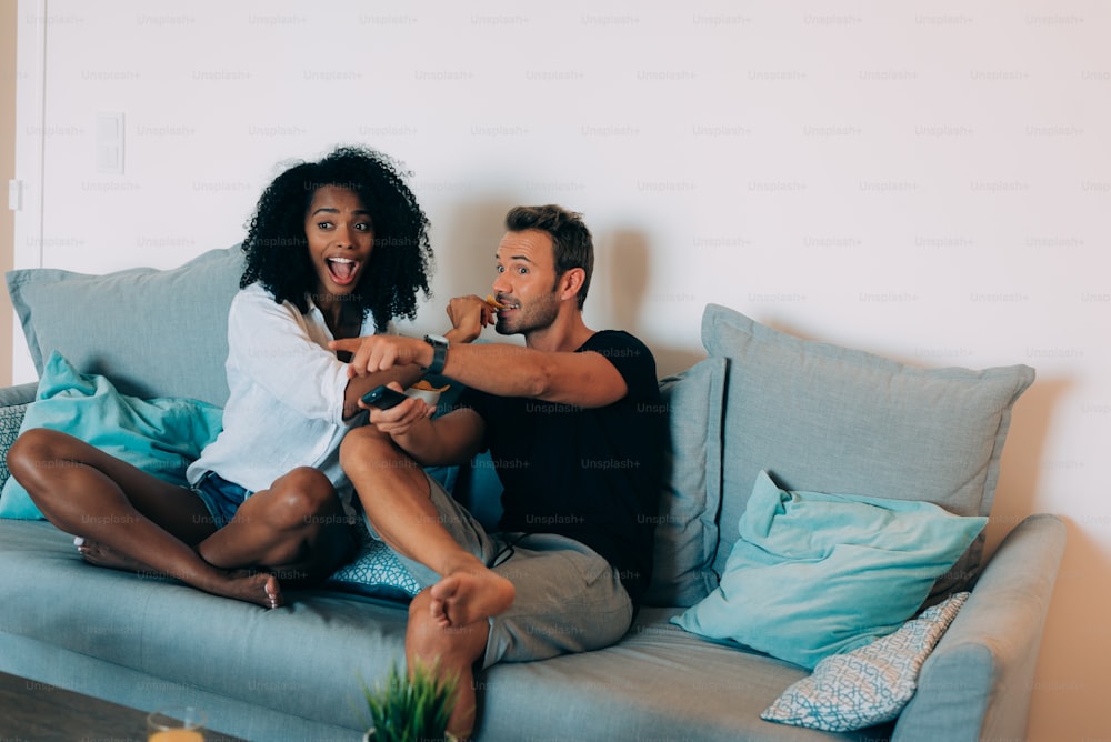 Glückliches junges Paar entspannt zu Hause auf der Couch und Spaß beim Fernsehen