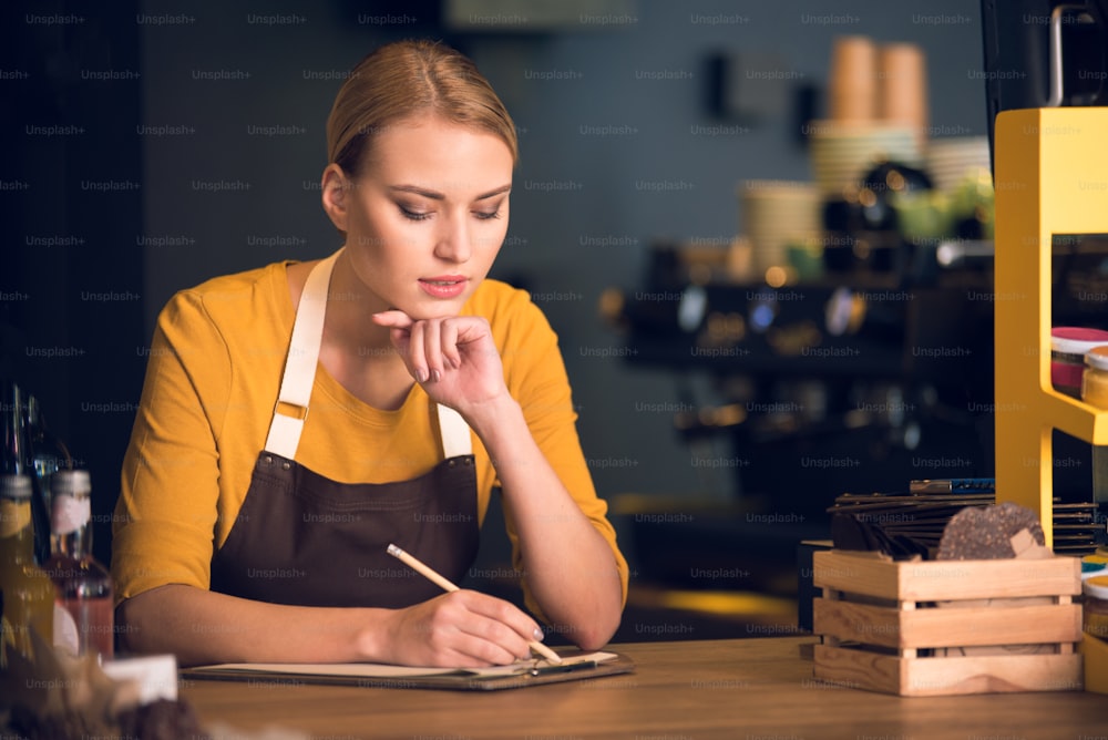 Portrait of serene worker filling information while situating at counter in comfortable cafe. Job concept