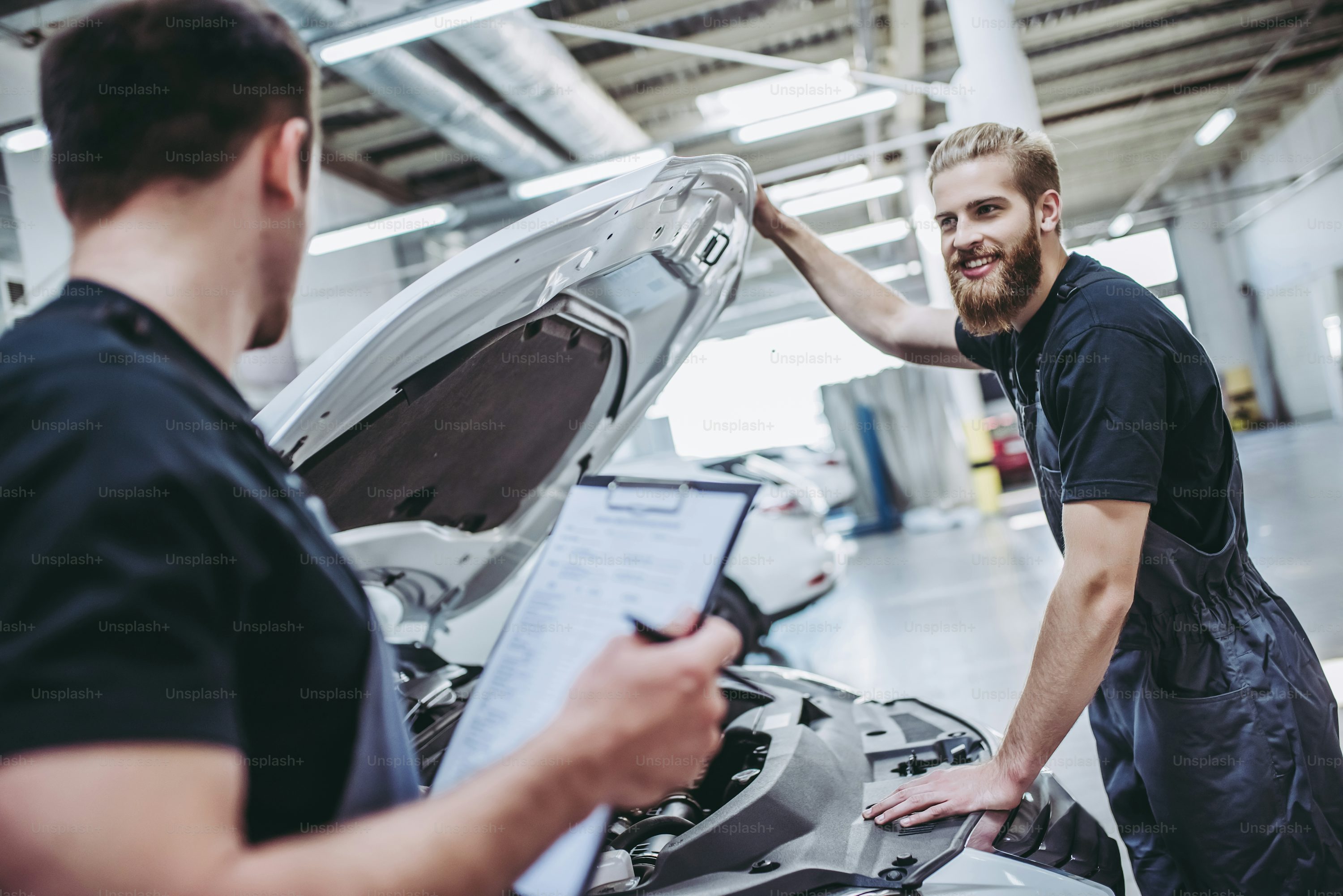 Two handsome mechanics in uniform are working in auto service. Car repair and maintenance.