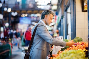 Guapo hombre de negocios maduro en una ciudad, comprando fruta a un vendedor. Fondo borroso.