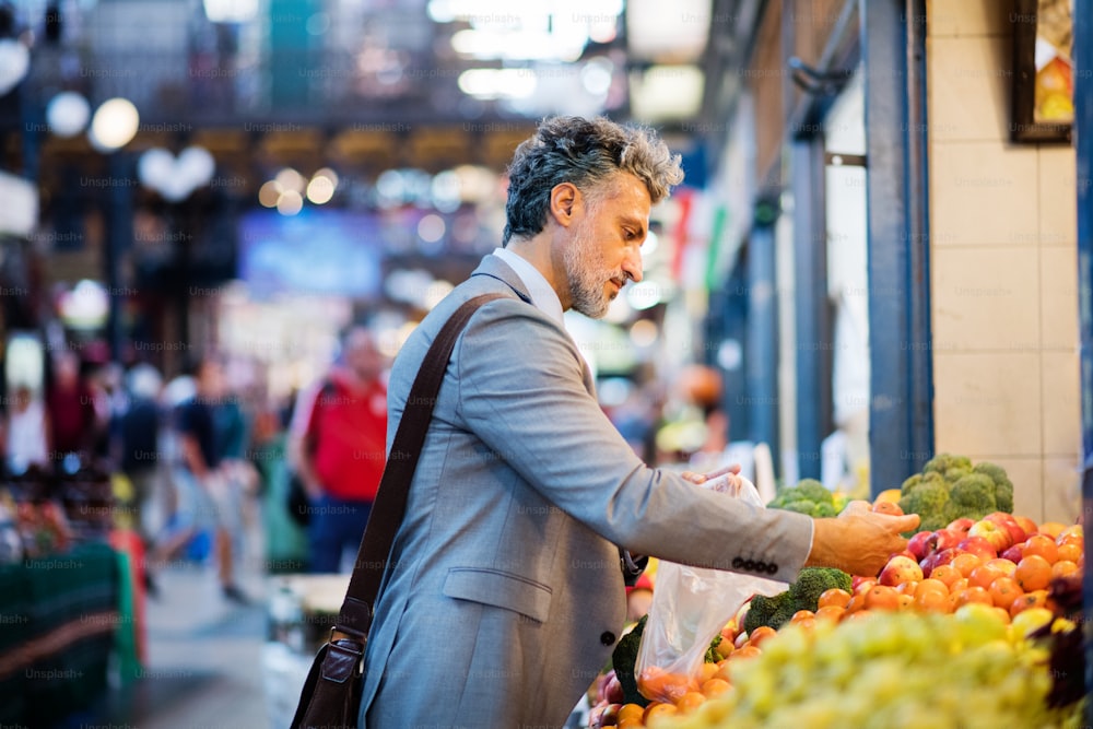 Handsome mature businessman in a city, buying fruit from a vendor. Blurred background.