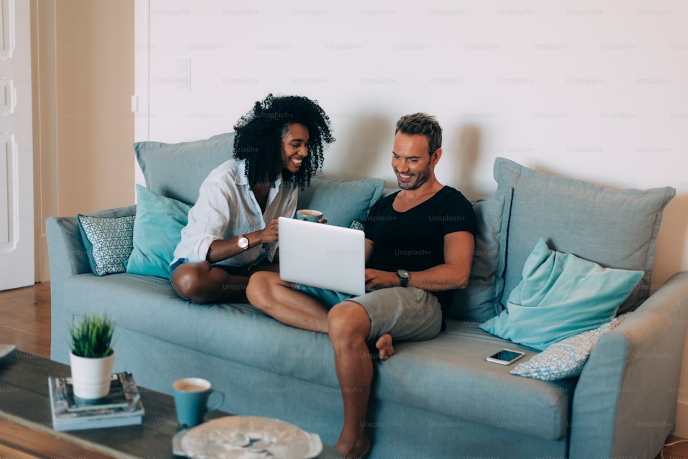 Glückliches junges Paar entspannt zu Hause auf der Couch auf Handy und Computer