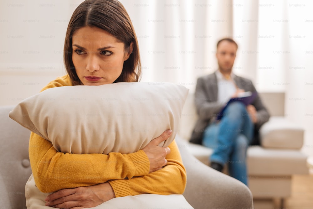 Therapy encourages. Attractive upset female patient  looking aside hugging cushion and crying