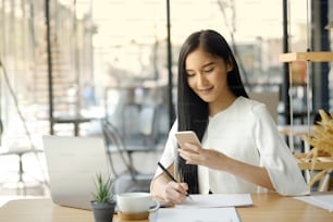 Portrait of a young asian woman sitting at her desk while using her mobile phone.