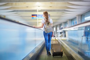 Belle jeune fille touriste avec sac à dos et bagages à main à l’aéroport international, sur le tapis roulant