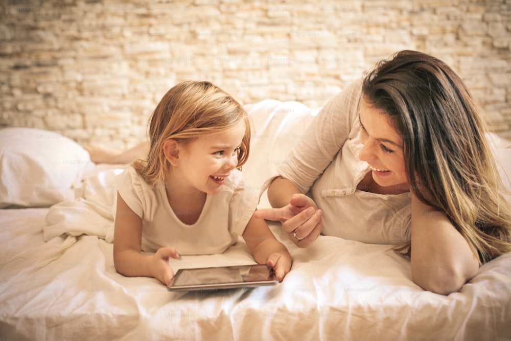 Mujer joven y su hija usando iPod en la cama.