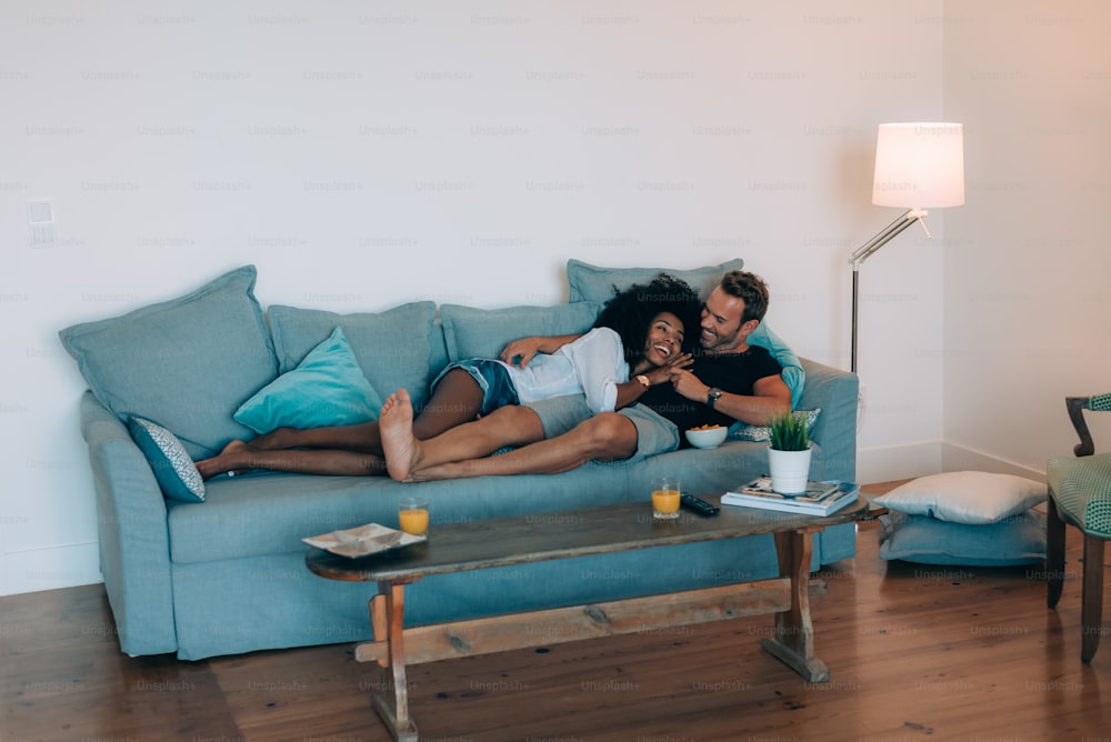 Feliz pareja joven relajada en casa en el sofá divirtiéndose viendo la televisión