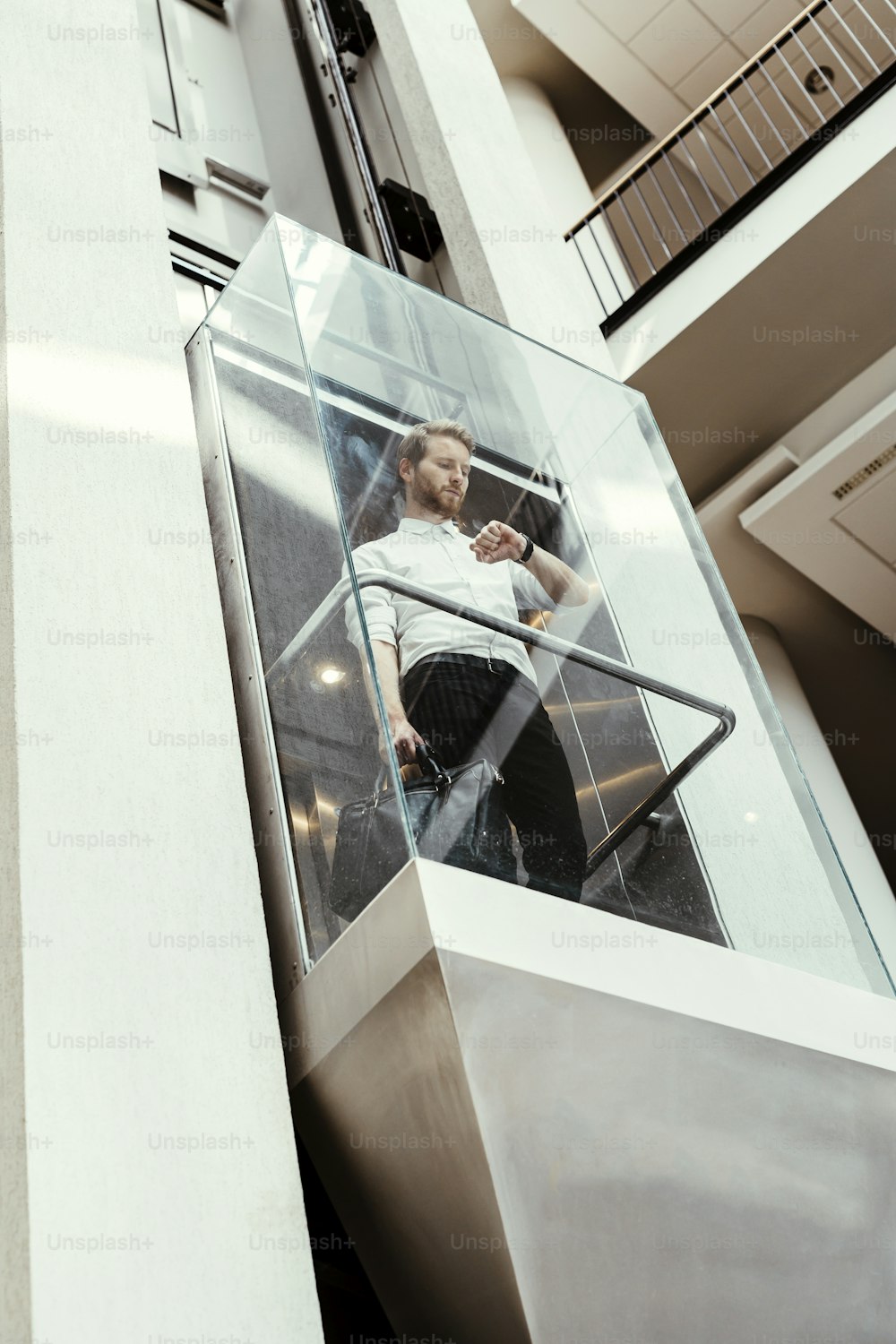 近代的なガラス張りのエレベーターで上層階へ向かうビジネスマン