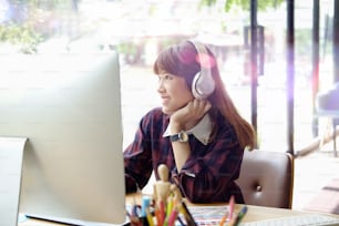 Mujer feliz usando una computadora de escritorio mientras escucha en la oficina del estudio.