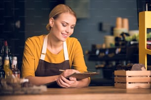 Portrait of cheerful woman worker noting information while resting elbows on table in cozy cafe. Occupation concept