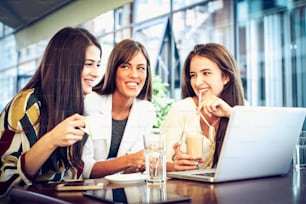 Three smiling woman in cafe with laptop.