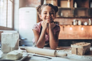 Little cute girl is cooking on kitchen. Having fun while making cakes and cookies. Smiling and looking at camera.