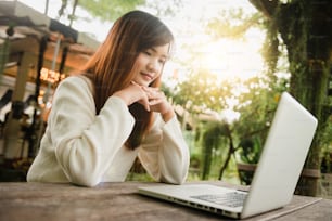 Imagem recortada da mulher jovem usando laptop no café. Close up retrato mulher asiática que trabalha no computador portátil, com foco no laptop. Mulher jovem asiática sentada no restaurante ocupado trabalhando no laptop