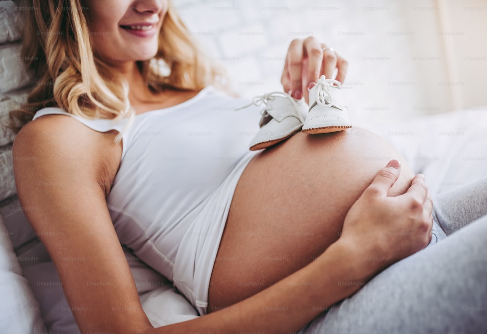 Une femme enceinte séduisante est allongée dans son lit avec de petites bottes sur le ventre. Derniers mois de grossesse.