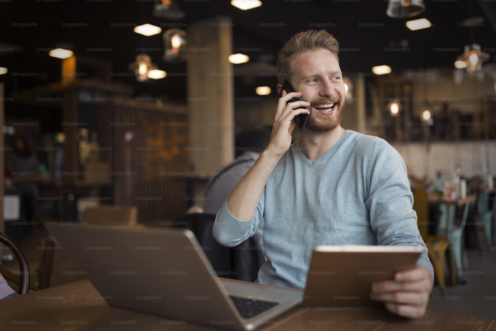 Young happy man having phone call in cafe holding tablet