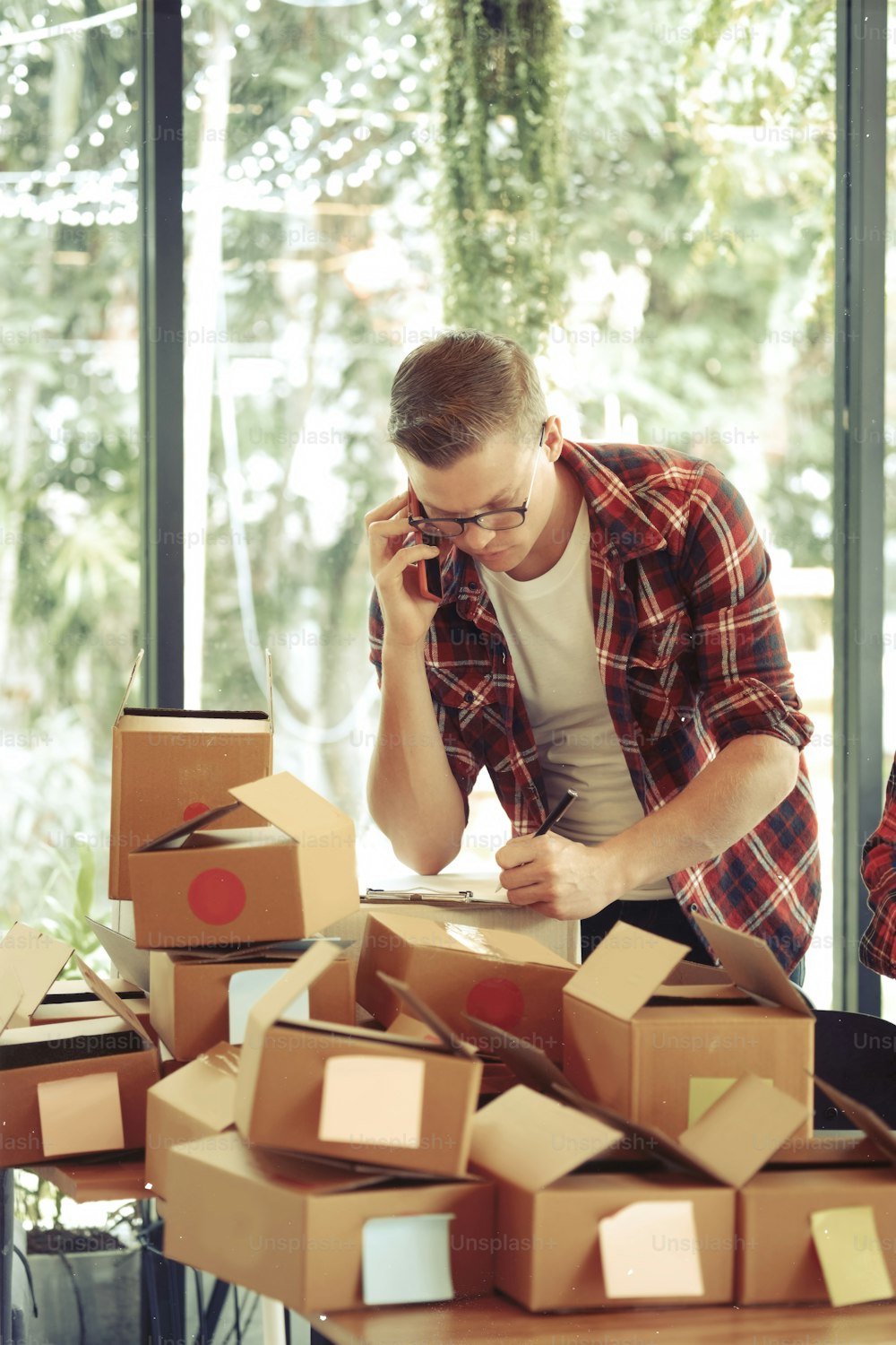 Shot of a man using mobile phone and packing cardboard boxes at home. Business online and delivery concept