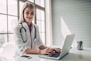 Attractive young female doctor is working with laptop in light cabinet. Smiling and looking at the camera.